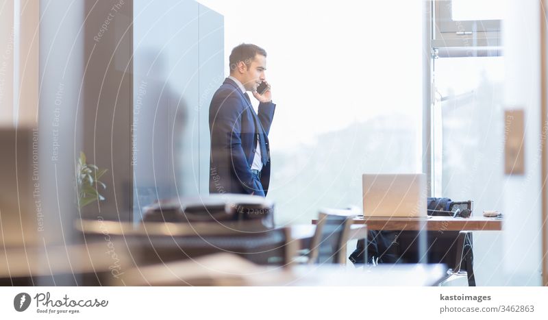 Geschäftsmann spricht mit einem Mobiltelefon, während er durch ein Fenster schaut. Business Telefon Büro korporativ Unternehmer professionell männlich Person