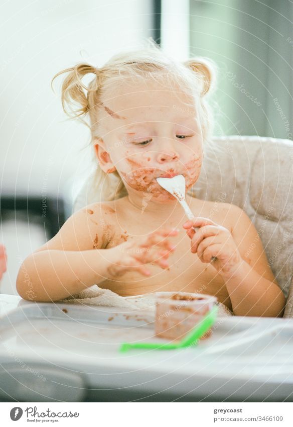 Es spielt keine Rolle, wie schmutzig das Gesicht ist, wenn es so lecker ist. Kleines Mädchen isst sitzend im Hochstuhl Kind dreckig unordentlich Esser essen