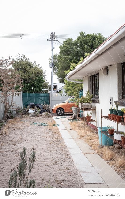 Ein etwas trostloser Vorstadthinterhof Hinterhof Garten kahl unordentlich leer sandiger Boden Haus Pflanzentöpfe Gartenschlauch PKW Zaun