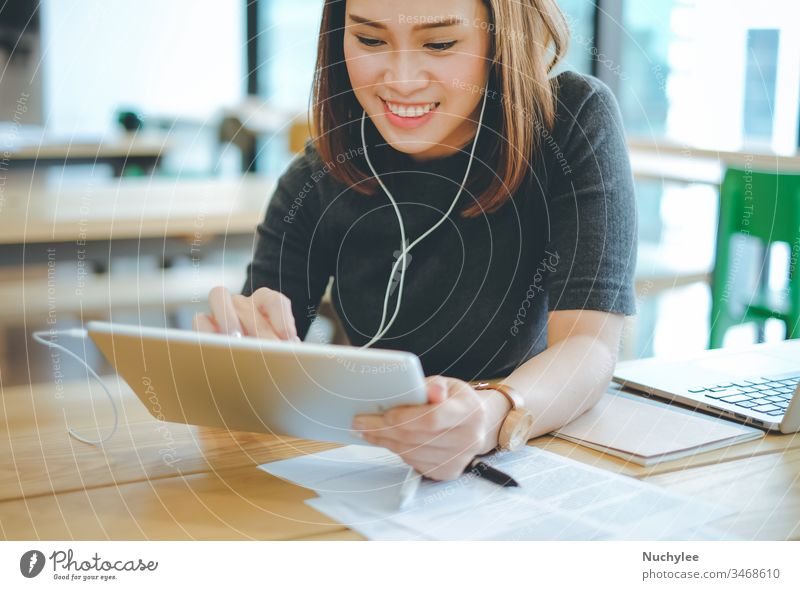 Junge lächelnde asiatische Geschäftsfrau, die im Büro oder Café Musik hört und Tablets benutzt, Lifestyle und Geschäftskonzept Business lässig heiter Großstadt