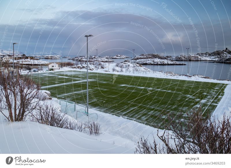 grünes Fußballfeld auf einer Insel im Meer in Schneelandschaft Henningsvær Lofoten Norwegen Skandinavien Winter Sportplatz Kunstrasen Austvagoya