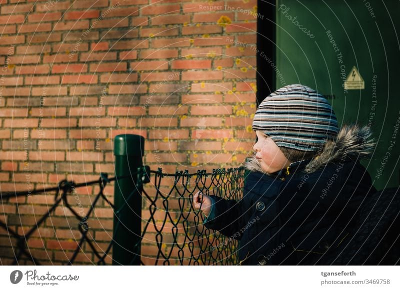 kleiner Junge schaut in die Ferne Kleinkind beobachten Maschendrahtzaun schauen sehen suchen. ausschau in die ferne sehen in die ferne schauen