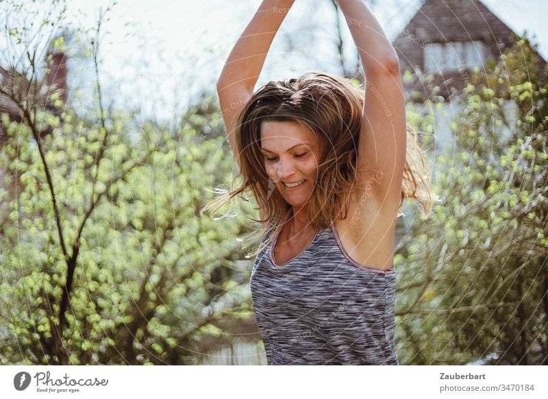 Schöne Frau springt mit erhobenen Armen im frühlingshaften Garten Frühling grün springen Sport Freude Lebensfreude schön Außenaufnahme Glück Bewegung feminin