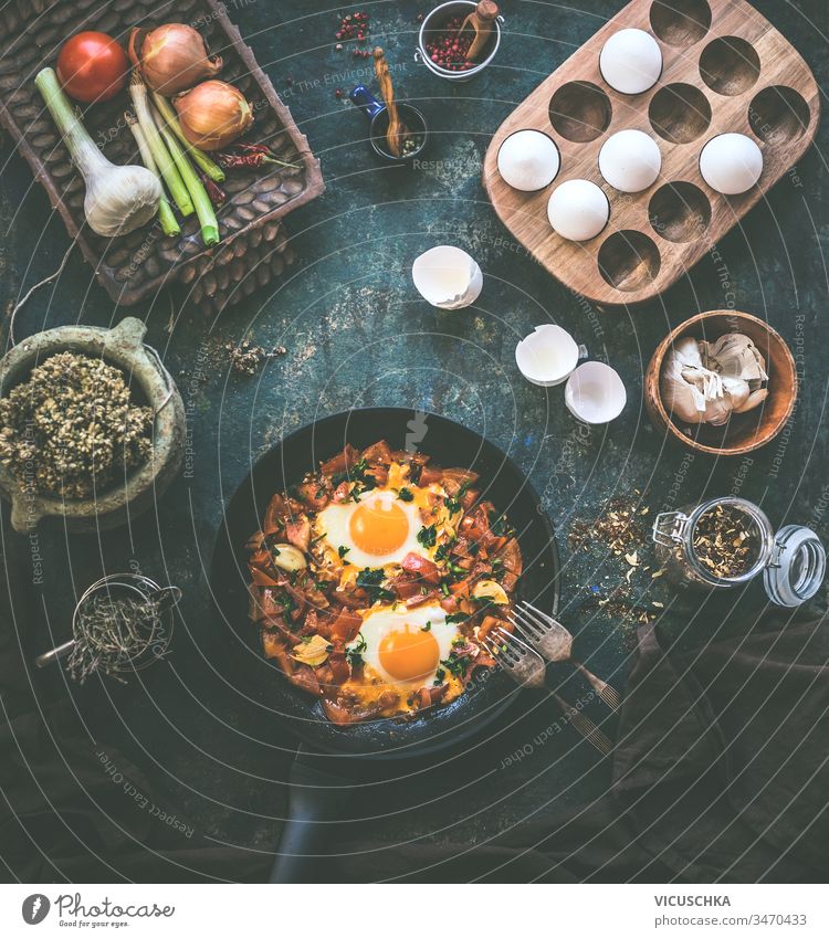 Schmackhafte Spiegeleier in Tomatensauce in schwarzer Pfanne mit Gabel auf rustikalem Hintergrund. Ansicht von oben. Shakshuka-Frühstück. Die Zutaten. Kochen. Gesunde Ernährung