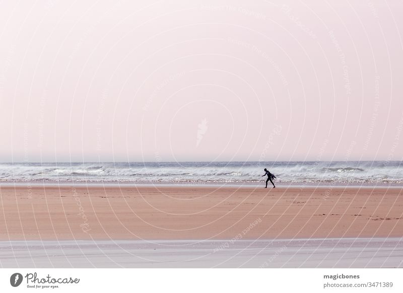 Einsamer Surfer mit einem Surfbrett an einem Strand in Cornwall, UK aktiv Aktivität Abenteuer atlantisch blau Holzplatte Küste Küstenlinie Tag England Spaß