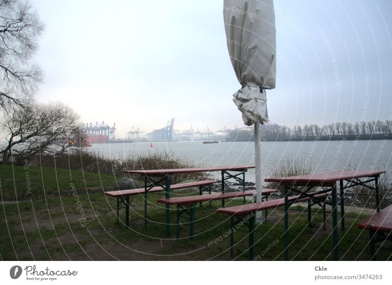 Bänke und Stühle am Elbufer, Blick auf Hafenanlagen Elbe Hamburg Gastronomie Sonnenschirm Fluss Gras Ufer Hamburger Hafen Kräne Lockdown Weite Wasser Strom