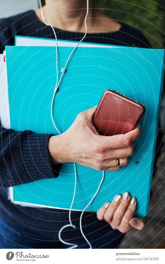 Frau, die aus der Ferne arbeitet und ihre Arbeit während eines Telefongesprächs von zu Hause aus erledigt. Frau hält Smartphone und Dokumente über Kopfhörer im Ordner