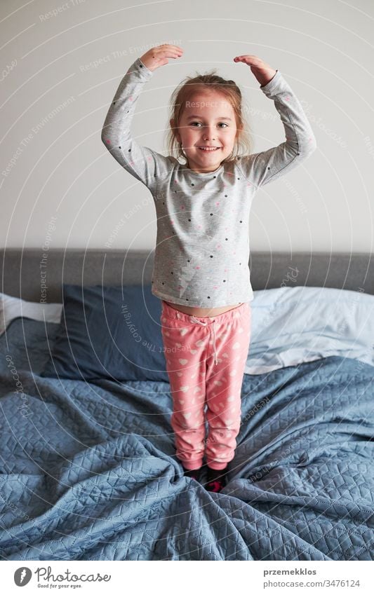 Kleines fröhliches, verspieltes Mädchen, das Spaß daran hat, morgens zu Hause im Schlafzimmer auf das Bett zu springen springend lustig Spielen Herstellung