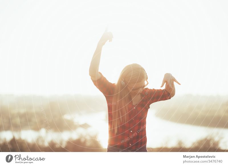 Junge Frau, die bei Sonnenuntergang im Freien mit Kopfhörern Musik hört jung hören außerhalb genießend Freude freudig Tanzen Drahtlos Technik & Technologie