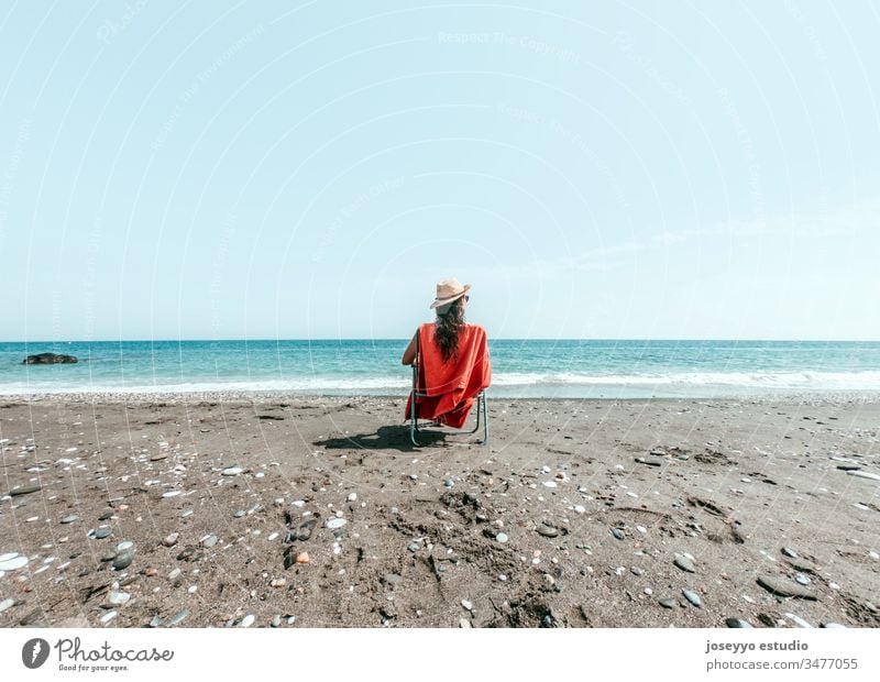 Mädchen mit Hut sitzt auf einem Liegestuhl mit orangem Handtuch am Strandufer Hintergrund schön blau Windstille Stuhl Küste Umwelt Frau Freiheit Behaarung