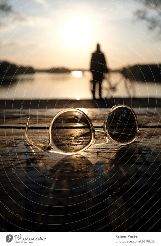 Entspannter Abend an einem See bei Sonnenuntergang, mit Sonnenbrille im Vordergrund Abenddämmerung entspannt Silhouette ruhig Ruhe Windstille Wasser Natur