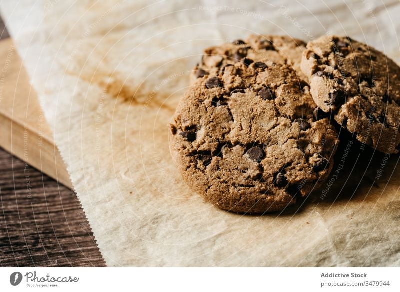 Leckere Schokoladenkekse auf Holztisch Keks hölzern gebacken Gebäck Biskuit süß Papier Lebensmittel Dessert dunkel geschmackvoll selbstgemacht Snack frisch