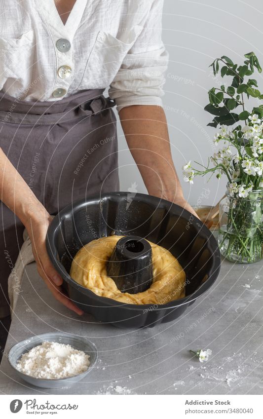 Nutzpflanzenfrau legt Teig in Bundtopf Frau Teigwaren Pfanne Bundkuchen Gebäck Koch Tisch Mehl Blume rollen Blumenstrauß Schürze Küche vorbereiten Lebensmittel