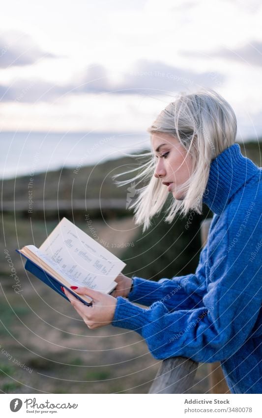 Junge Frau liest Buch am Meer MEER Zaun Strand ruhen lesen jung blau genießen Poesie Pullover Natur sich[Akk] entspannen hölzern Stil allein modern trendy blond