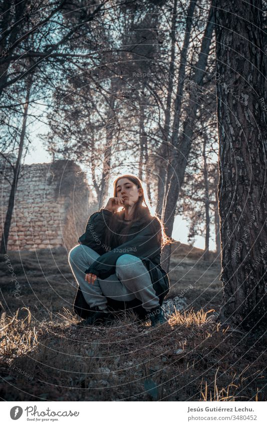 junges Mädchen mit ernstem Blick auf dem Gras sitzend mit starkem Kontrast im Hintergrund zur Sonne Vorderansicht Oberkörper Farbfoto Leben Spanien retro