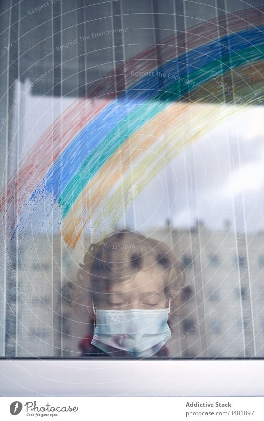 Junge hinter Fenster während der Quarantäne Mundschutz medizinisch Regenbogen farbenfroh heimwärts Krankenhaus Stirnrunzeln Pandemie Coronavirus Bund 19 Kind