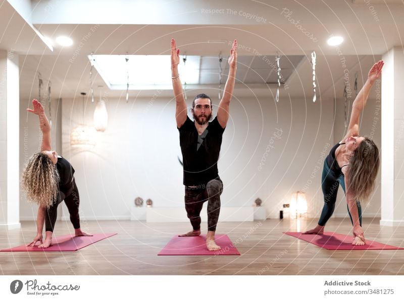 Gruppe von Menschen, die beim Yoga die Kriegerhaltung und die erweiterte Seitenwinkelhaltung einnehmen Frauen strecken Mann Raum Handreichung Krieger-Pose