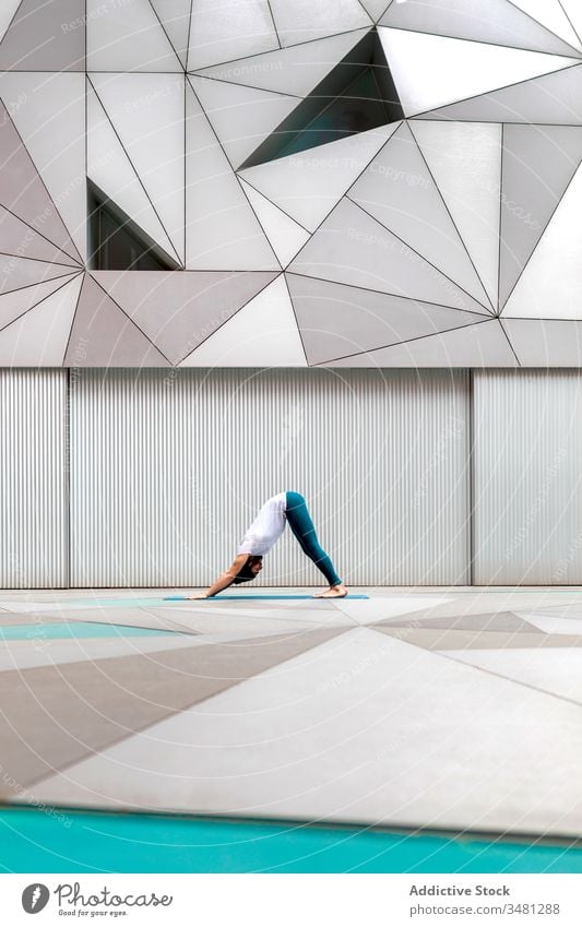 Mann macht Yoga in geräumigem Raum Übung Training Geometrie nach unten gerichtete Hundehaltung modern Dehnung Fitness Form männlich Sportbekleidung Architektur