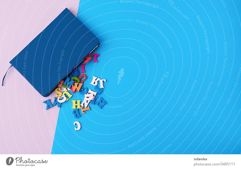 blaues Notizbuch und verstreute mehrfarbige Holzbuchstaben auf einem abstrakten Hintergrund farbenfroh oben blanko Business zugeklappt Farbe Konzept kreativ