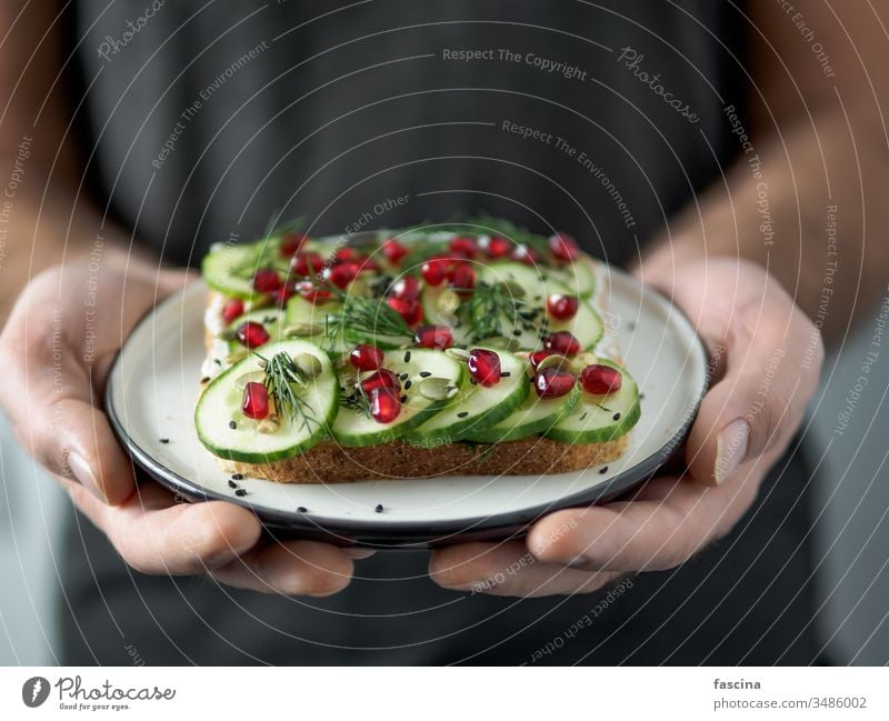 Veganes Sandwich mit Gurke in Männerhänden Belegtes Brot Veganer Hand Zuprosten Veggie Teller pflanzlich Salatgurke Granatapfel verzehrfertig Ideen Gesundheit