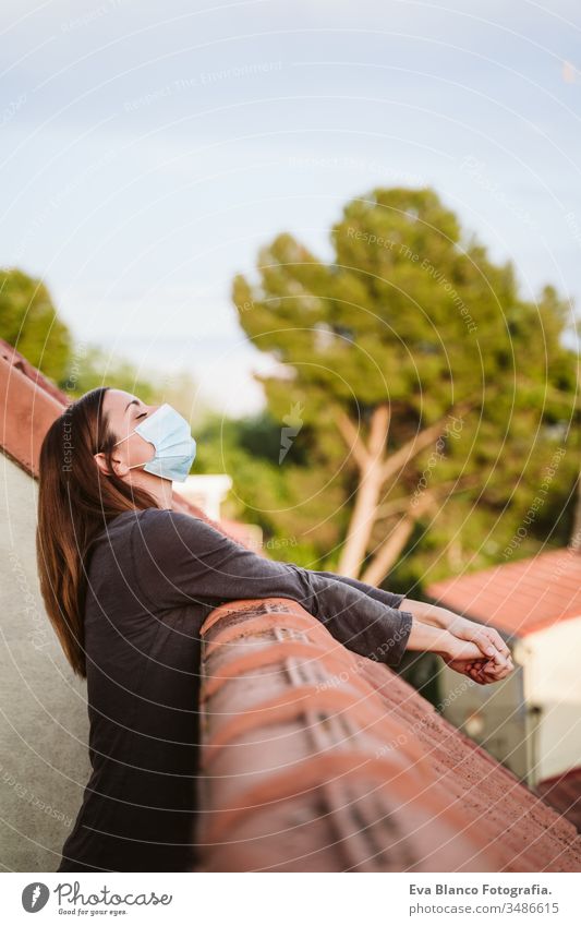 junge Frau zu Hause auf einer Terrasse, die eine Schutzmaske trägt und einen sonnigen Tag genießt. Coronavirus Covid-19-Konzept covid-19 schützend Mundschutz