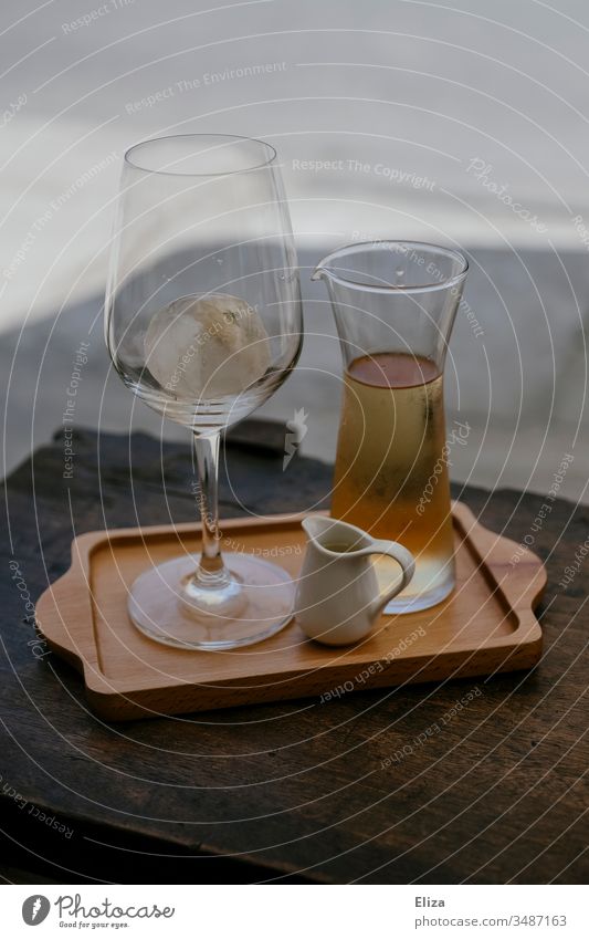 Ein Tablett mit einem Glas und einer Karaffe gefüllt mir einer hellen Flüssigkeit Weinglas Eistee Eiswürfel Sommer draußen servieren Gastronomie edel Alkohol