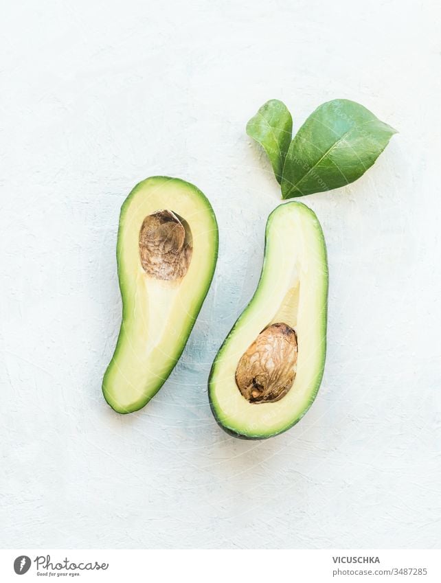 In zwei Hälften geschnittene Avocado mit grünen Blättern auf weißem Tischhintergrund, Ansicht von oben. Gesunde Lebensmittelzutat Hintergrund Draufsicht