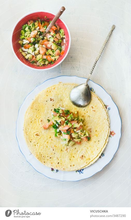 Tortilla umhüllt die Zubereitung von Sandwiches mit leckerem frischen Avocado-Salsa-Salat auf weißem Hintergrund, Draufsicht. Gesundes Essen.  Vegetarisches Mittagessen oder Snack