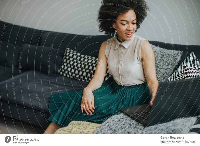 Junge schöne Dame mit lockigem Haar arbeitet am Notebook, während sie zu Hause auf der Couch sitzt jung Laptop Computer Frau Sofa heimwärts Person arbeiten