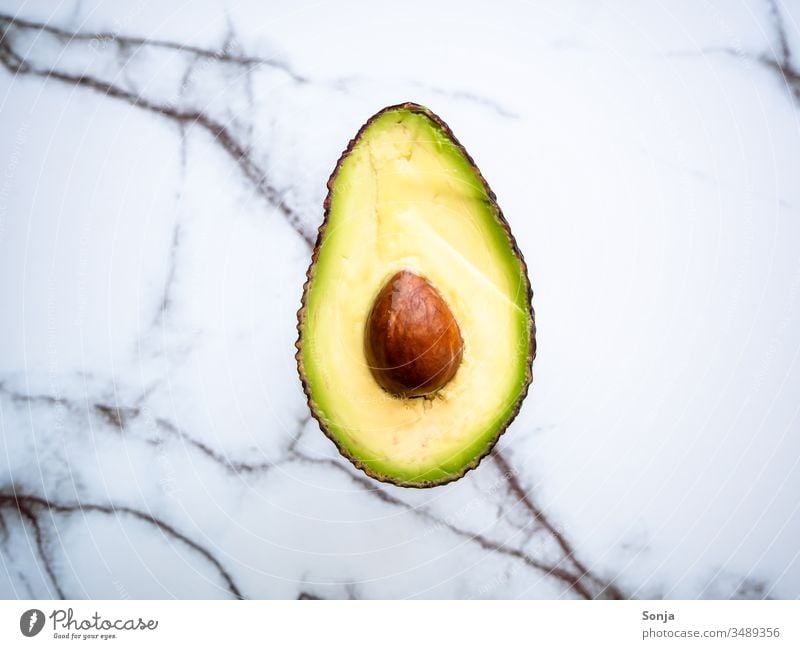 Halbierte Avocado mit Kern auf einem Marmorhintergrund, Draufsicht halbiert Avocadokern draufsicht Lebensmittel Gesunde Ernährung Vegetarische Ernährung frisch