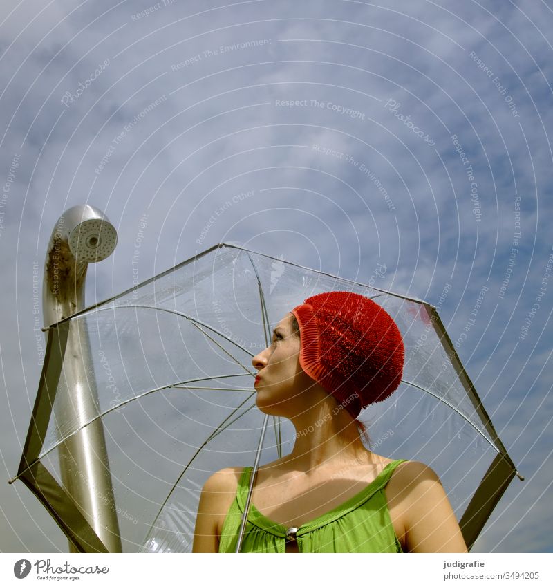 Das Mädchen mit der schönen roten Badekappe, grünem Badeanzug und Regenschirm schaut verwundert auf die Dusche. Eine Sommerliebe. Frau Badebekleidung Badehaube