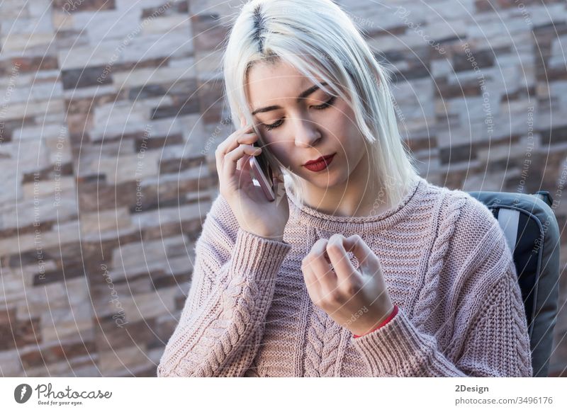 Junge, hübsche Frau, die auf dem Sofa auf der Terrasse sitzt und telefoniert 1 Mobile Handy sprechend Telefon heimwärts im Freien Freizeitkleidung Erwachsener