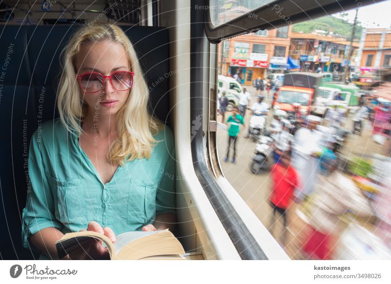 Blonde kaukasische Frau liest im Zug am Fenster ein Buch. reisen lesen Transport adveture Reise im Innenbereich entspannend Seitenansicht Urlaub in Bewegung