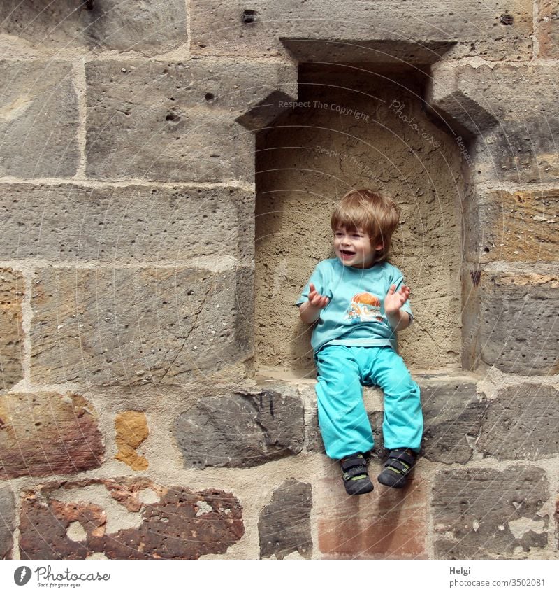 lachender kleiner Junge sitzt in einer Mauerlücke und scheint zu sagen " und nun...? " Mensch Kind Kleinkind männlich Porträt jung Lachen Fröhlichkeit Freude