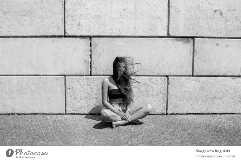 schneidersitz Schwarzweißfoto Mitte sitzen Schneidersitz langhaarig Haare & Frisuren dünn Frau Mädchen Mauer Stein Beton Wind Wärme Sommer trist modern Mode