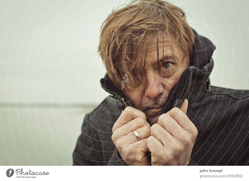 Huschi Haarsträhne Mann Porträt Mensch Blick kalt frieren Frost Winter See Gewässer verwegen Außenaufnahme Mantel Blick in die Kamera bad hair day Strubbelig