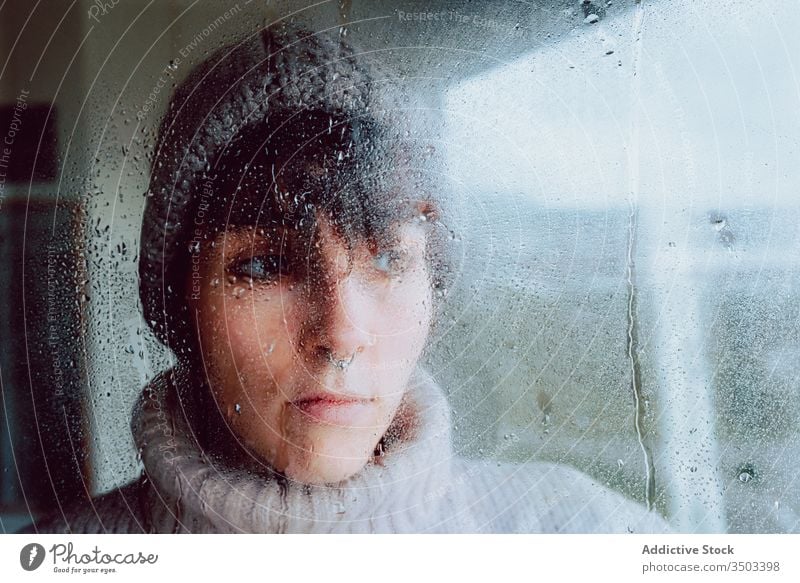 Melancholische junge Frau schaut durchs Fenster traurig Depression Isolation Coronavirus heimwärts verzweifelt einsam unglücklich männlich nass Regen