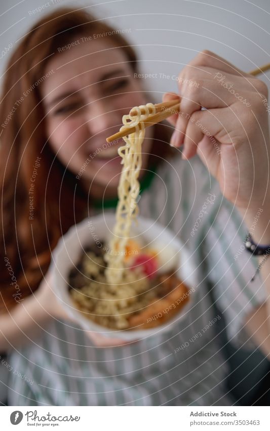 Glückliche Frau isst zu Hause Nudeln essen Ramen heimwärts Japanisch Sofa Essstäbchen jung Rotschopf heiter Lebensmittel Tradition authentisch asiatisch