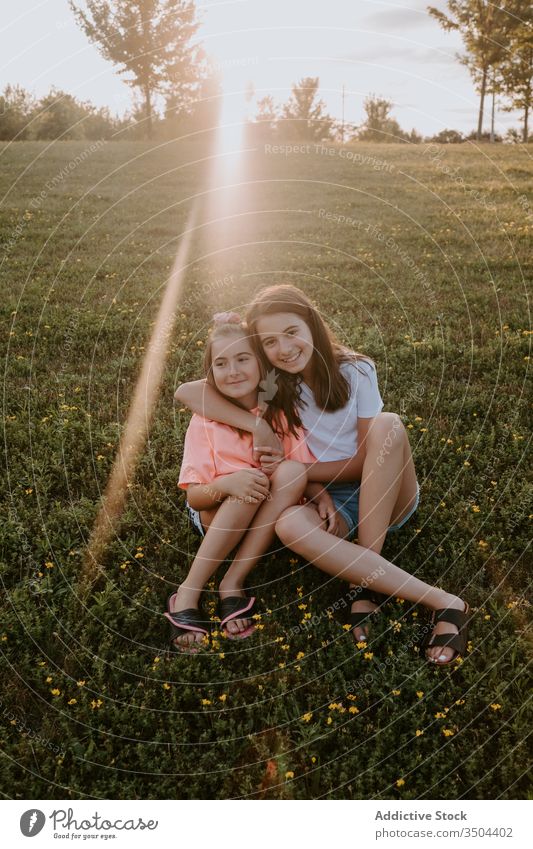 Glückliche Kinder, die sich auf der grünen Wiese umarmen Schwester Natur Zusammensein Umarmung sitzen Gras Sommer Mädchen Landschaft heiter Teenager