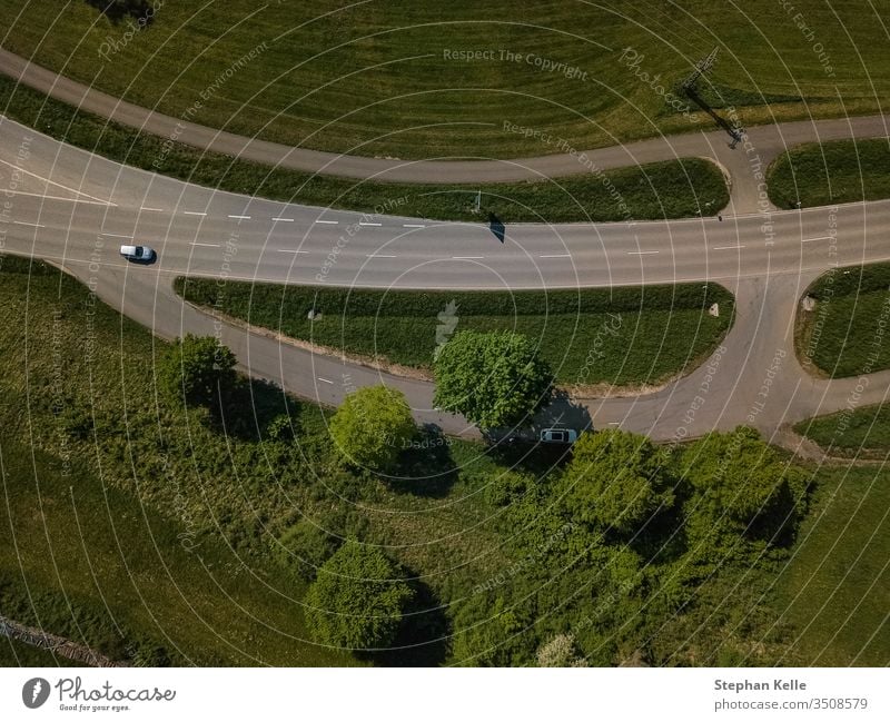 Senkrechter Blick nach unten auf eine Straße mit angrenzendem Parkplatz im Grünen. straße drohne auto von oben rasen wiese PKW grün Verkehr Landschaft Farbfoto