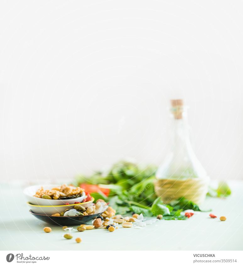 Gesunde Salatzubereitung auf weißem Tisch vor hellem sonnigen Wandhintergrund. Frische Küchenkräuter. Nüsse als Garnierung. Olivenöl. Salatdressing . Konzept für Diät oder vegetarisches Essen.