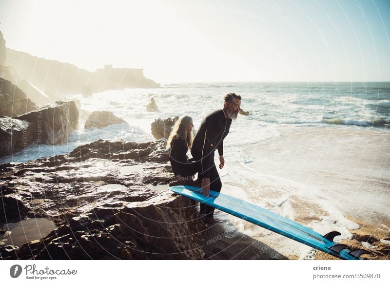 Älteres Ehepaar sitzt zusammen auf Felsen mit Surfbrettern und macht eine Pause Paar Zusammensein Senior Männer Urlaub Strand Surfen Erwachsener Vollbart