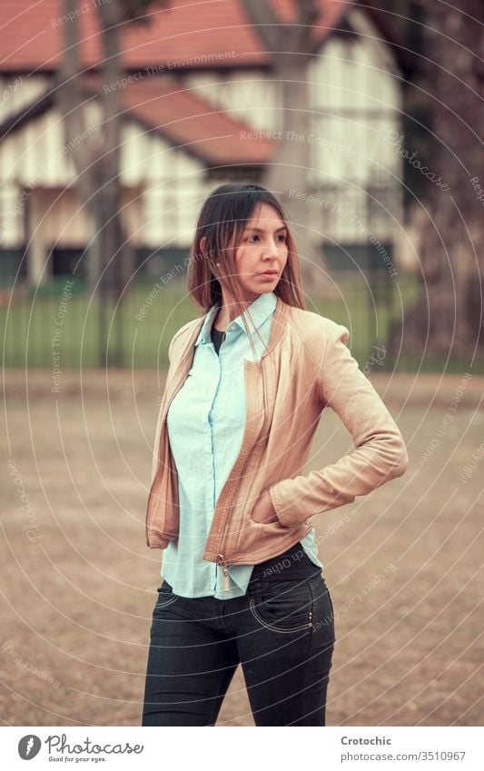 Frau steht auf der Straße mit abgewandten Händen in Lederjacke vertikal Porträt jung Mädchen feminin Haus Gebäude Park Baum Natur Herbst drehen. Verkleidung