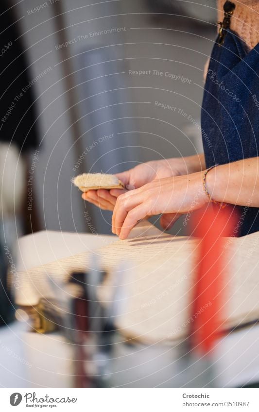 Vertikales Foto einer Frau, die ein Buch mit einem Pinsel repariert alt antik Hand Person Arbeiter Reparatur Sauberkeit Bürste weich Pflege vertikal