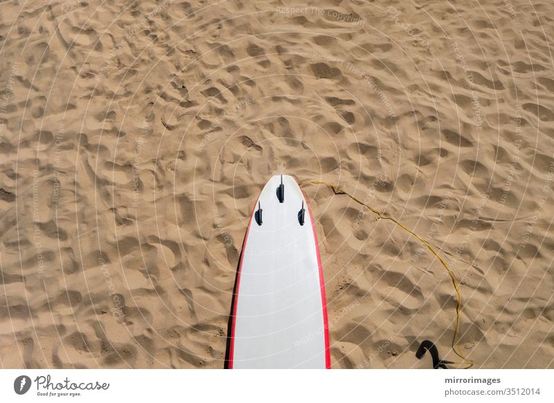 Thruster 3-Flossen-Rückseite eines Shortboard-Surfbretts mit weiß-rotem Nadelstreifen auf Sandstrand mit Fußabdrücken shortboard funboard Triebwerk drei Flosse