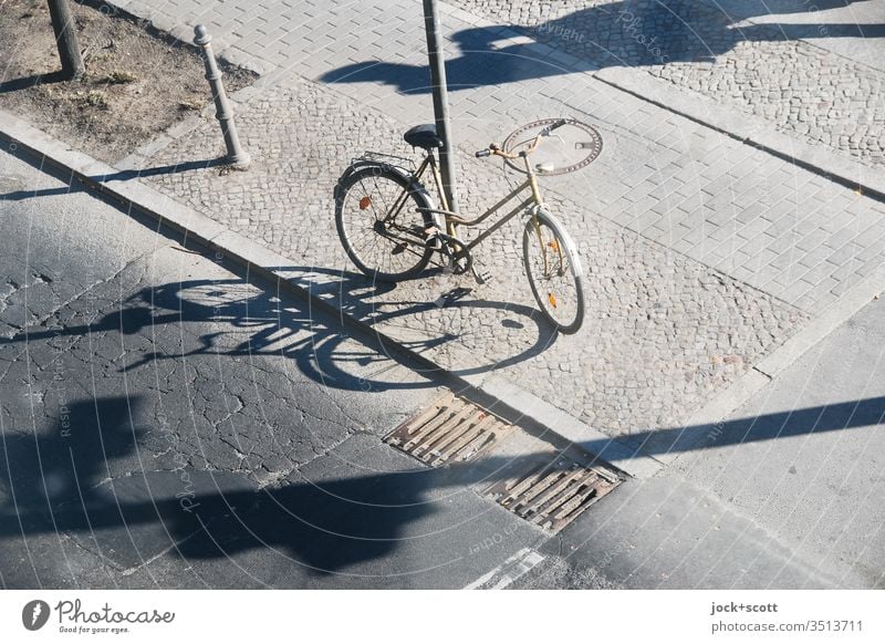 mit langen Schatten zentral abgestellt Fahrrad Asphalt Straße Verkehrswege angeschlossen Pfahl Bürgersteig Kopfsteinpflaster Risse Bordsteinkante abstrakt Gully