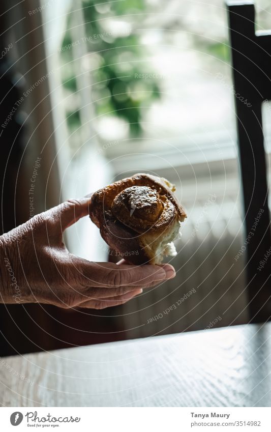 Hand einer Frau, die ein Zimtbrötchen hält Zimtkuchen Zimtschnecke Essen Kinderspiel Kuchen Spielfigur Brot Foodfotografie Menschen natürliches Licht