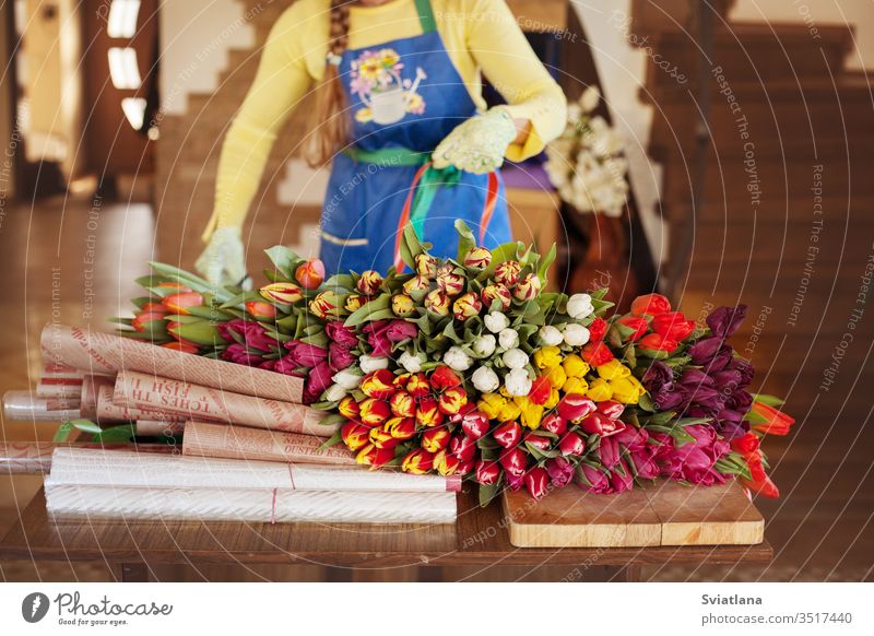 Eine Blumenhändlerin verpackt in einem Blumenladen schöne Tulpen in Kraftpapier. Frauentag und Valentinstag Blumenstrauß Hände Papier Ansicht rosa Verpackung