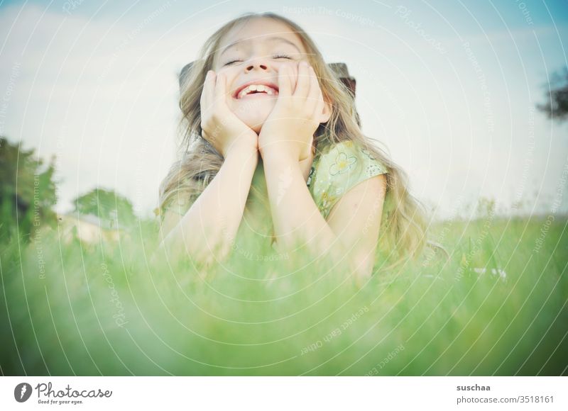 mächen liegt auf aufgestützten armen im gras und lacht Kind Mädchen Kindheit Freude lachen Lebensfreude Spaß Leichtigkeit Gesicht Hände Gras liegen Lächeln