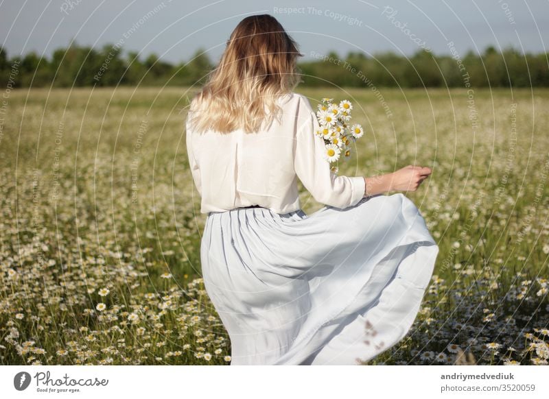 stilvolle junge blonde Frau, die an einem sonnigen Sommertag in einem Feld mit Gänseblümchen spazieren geht. laufen Margeriten Blumen Wiese Natur Menschen Glück